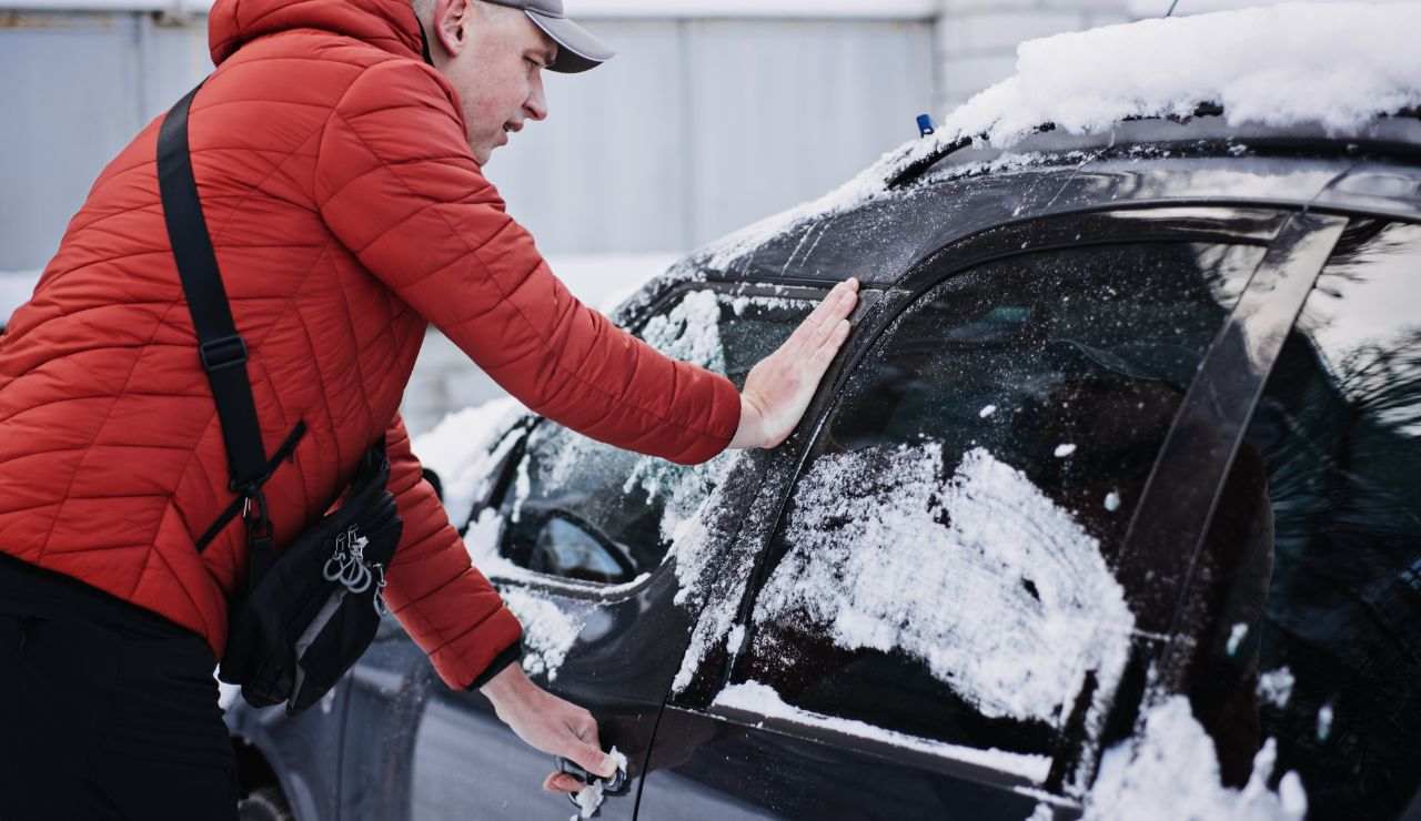 Uomo con giubbotto rosso apre lo sportello dell'auto ghiacciata